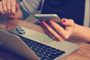 woman holding iphone while working at laptop