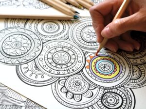 a womans hand holds a colored pencil while coloring a mandala coloring page