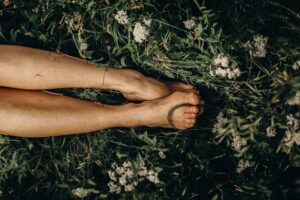 a womans feet and legs laying in the grass surrounded by flowers