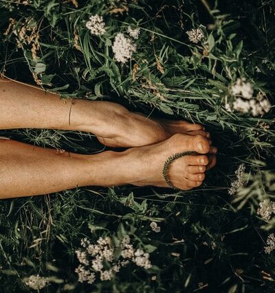 a womans feet and legs laying in the grass surrounded by flowers