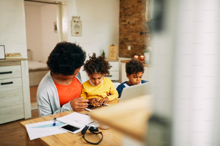 woman sitting at a kitchen counter with her two children looking at a tablet